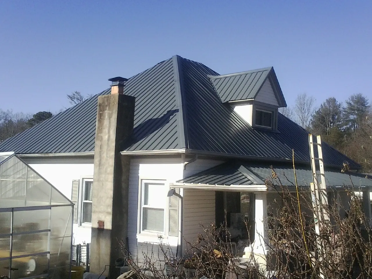 Dark blue standing seam metal roof on a white farmhouse with dormer — Slate & Tile Roof Repair by Roofing Brothers in Vail