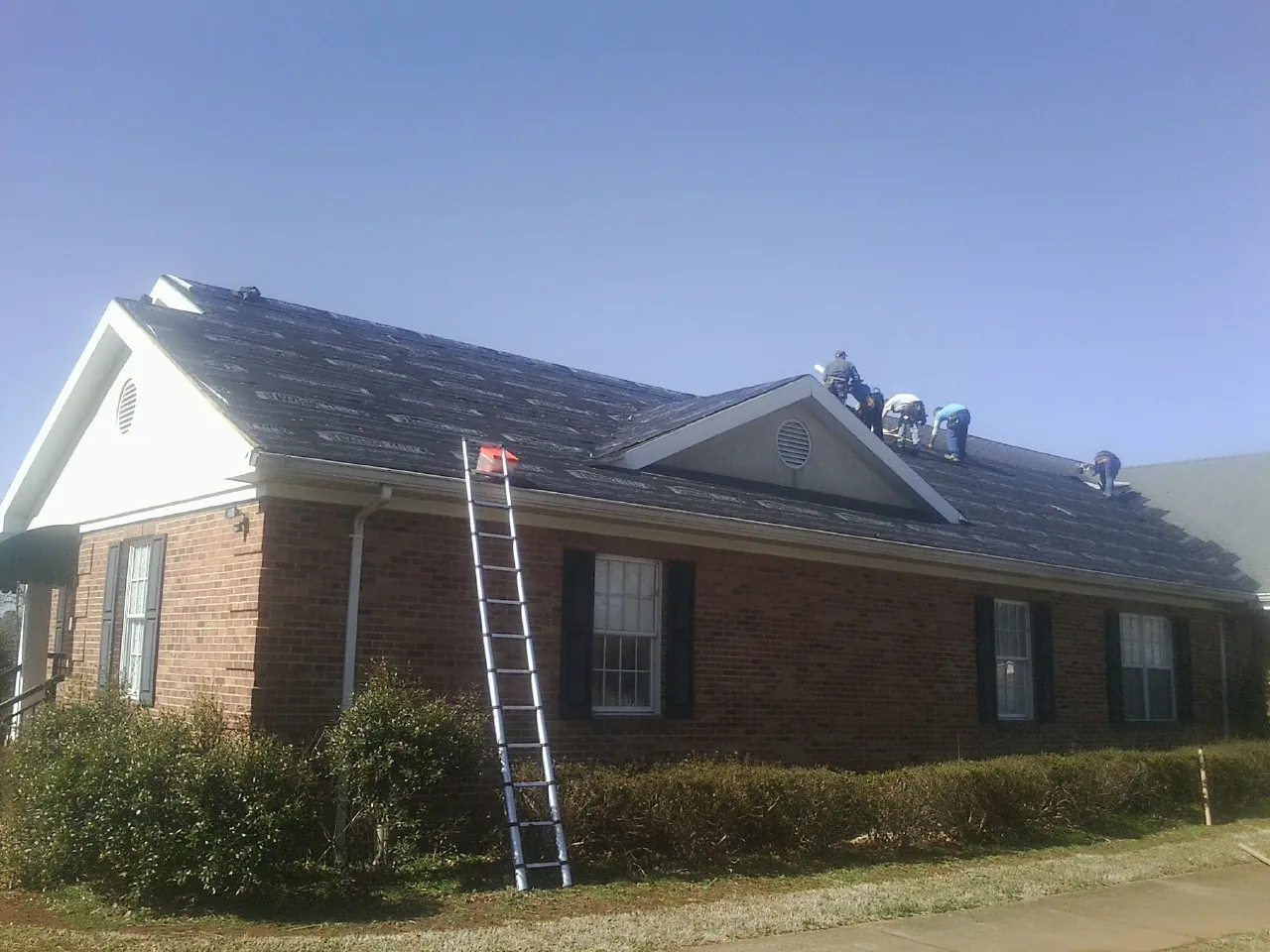 Crew tearing shingles off a brick ranch roof with a ladder set — Emergency Roof Repair work by our crew in Vail