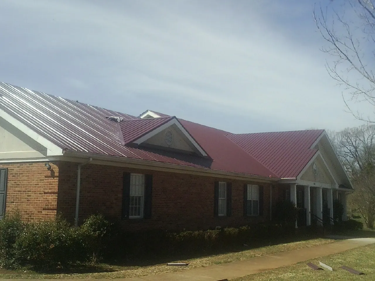 Red metal roof with gabled entries on a long brick building, from a Hail Damage Roof Repair job in Vail