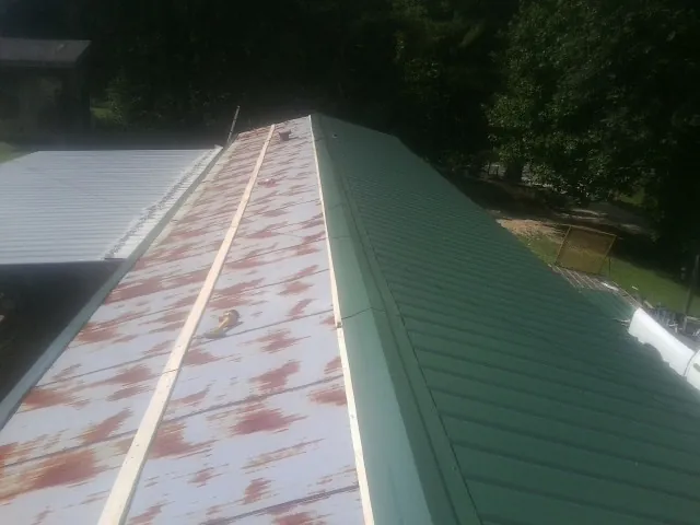 Old rusted panels beside newly installed green metal roofing — Wind Damage Roof Repair by Roofing Brothers in Vail