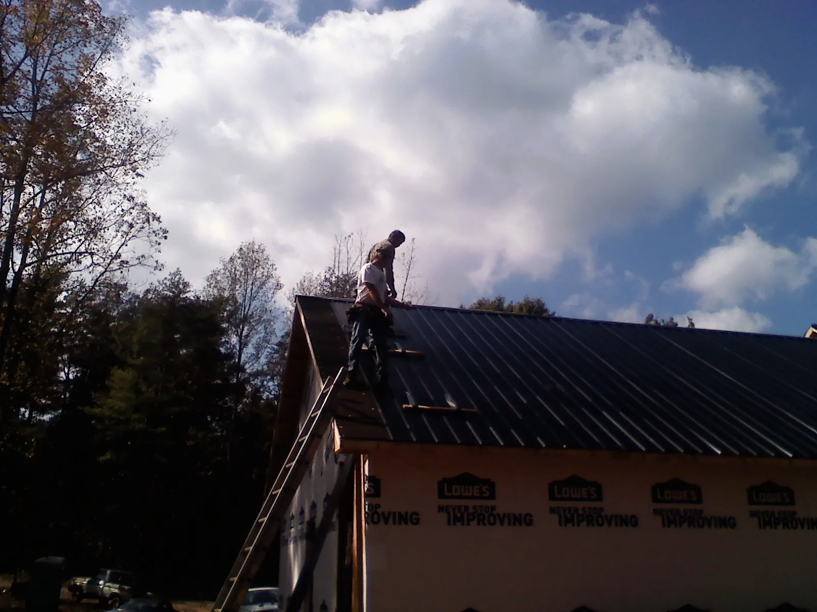 Roofer fastening dark metal panels high against a cloudy sky, from a Roof Inspection job in Vail
